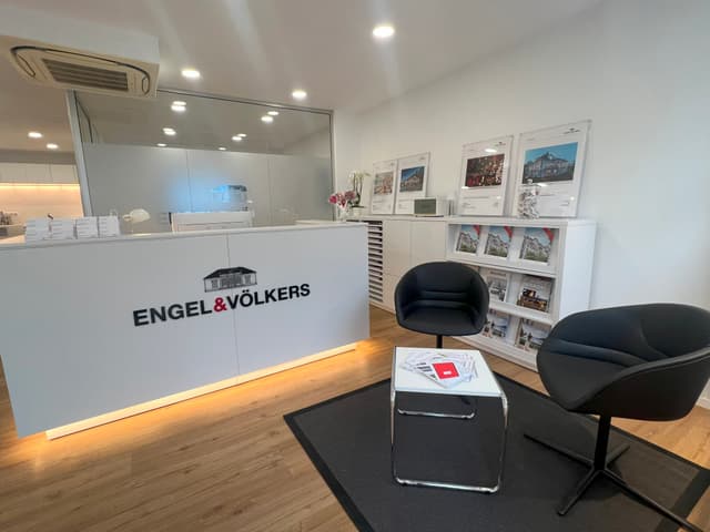 Engel & Völkers real estate office with a white reception desk, black chairs, and a table with brochures.