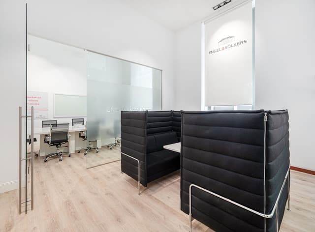 Engel & Völkers Bürointerieur mit schwarzen Sitzecken, einem Konferenzraum mit Glaswänden und hellen Holzböden.